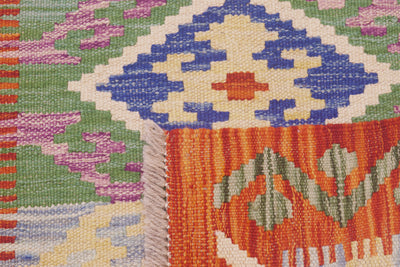 Close-up of the weave of a  handwoven Afghan Kilim runner with a multicolour geometric pattern, showing orange, blue, green, cream, and pink sections with visible fringe.