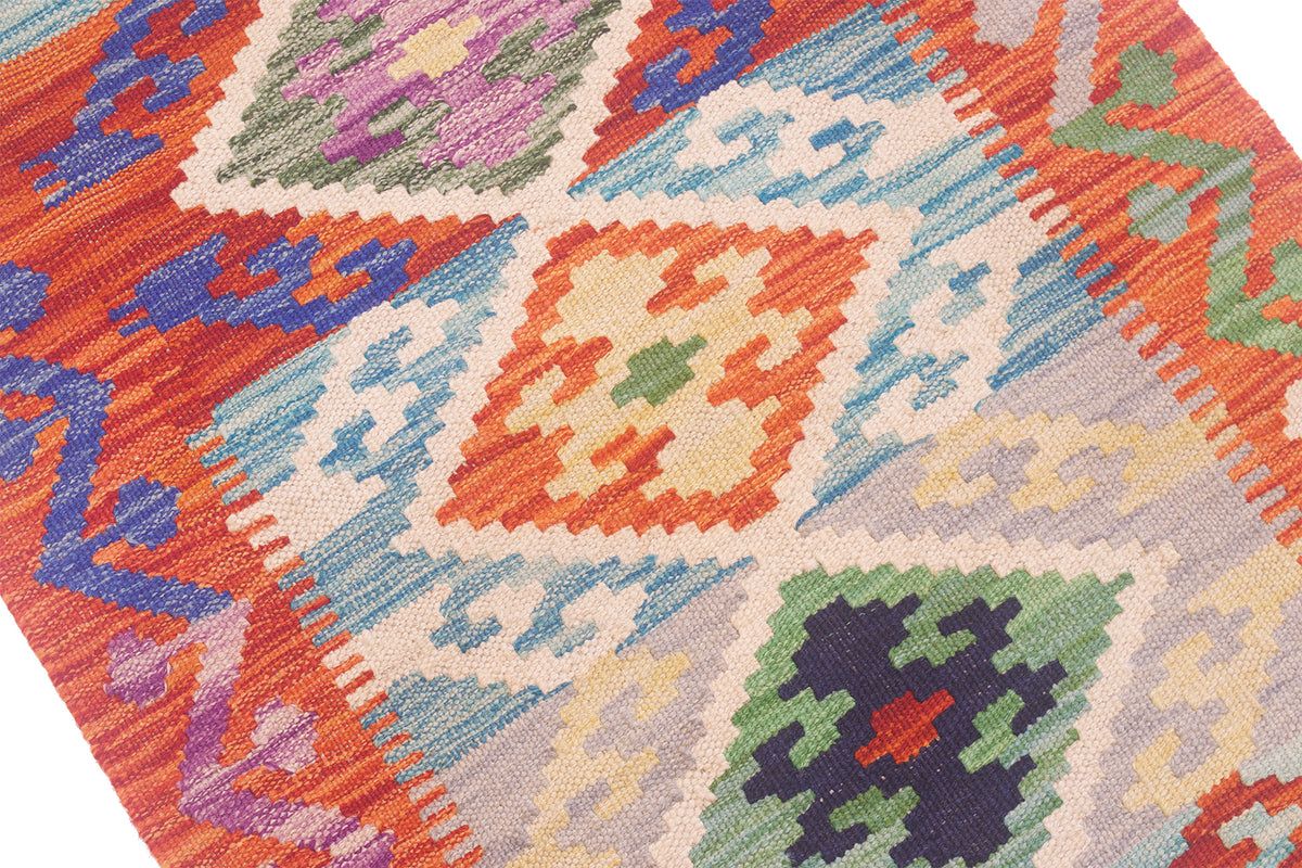 A close-up of a colourful woven Kilim short runner with geometric diamond patterns in orange, blue, cream, green, purple, and red.