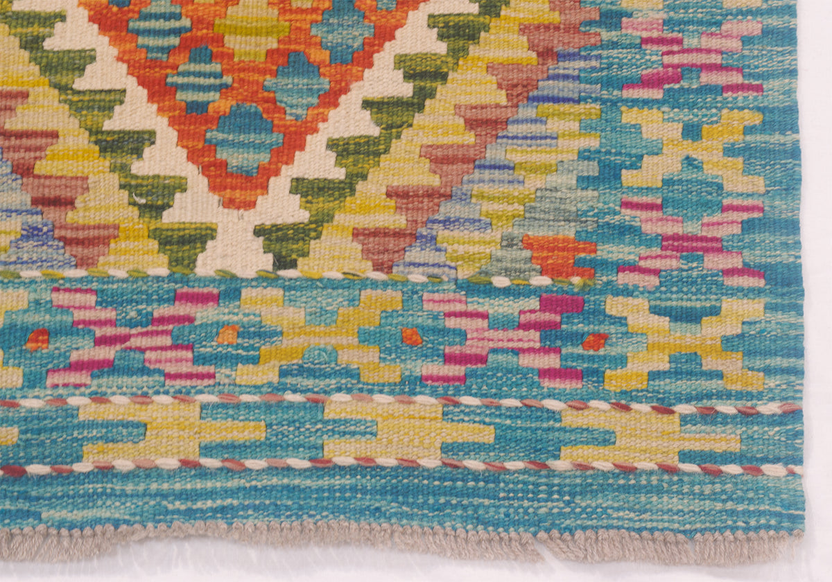 Close-up of a woven kilim runner showing a colourful geometric pattern with turquoise blue, yellow, pink, orange, and cream stripes and diamond motifs.