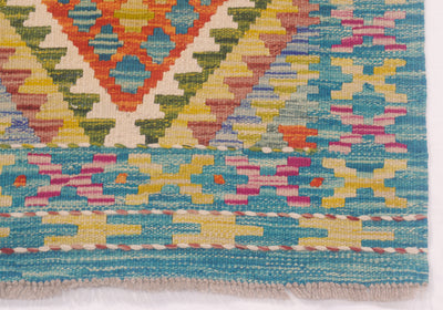 Close-up of a woven kilim runner showing a colourful geometric pattern with turquoise blue, yellow, pink, orange, and cream stripes and diamond motifs.