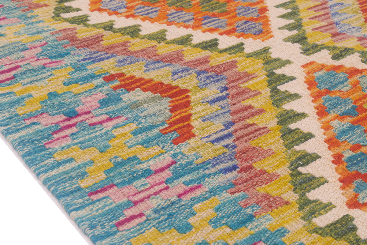 A close-up of a colorful geometric patterned kilim runner with a textured, woven surface. The design features a mix of blue, yellow, pink, orange, green, and beige in a repeating tribal or kilim-inspired motif.