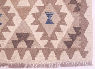 Close-up of a woven Afghan Natural Dye Kilim Runner with a geometric diamond pattern in beige, taupe, brown, and a small blue accent near the top center, with fringe visible along the bottom edge.