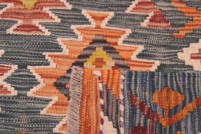 Close-up of a large handwoven kilim rug showing a geometric pattern with orange, dark green, cream, and rust tones.