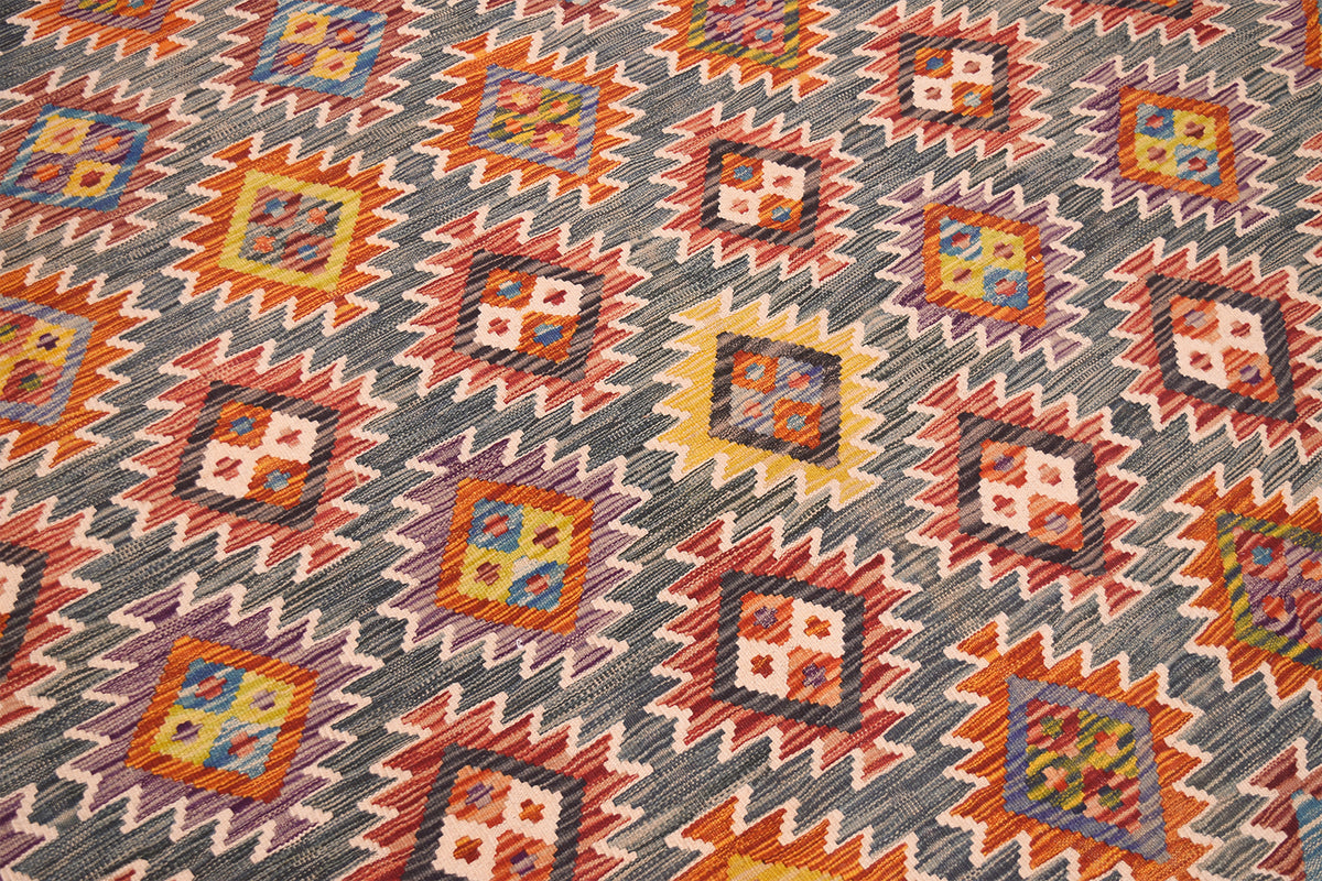 A close-up of a handwoven large Kilim rug with a geometric kilim pattern in green, orange, red, yellow, and blue.