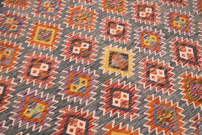 A close-up of a handwoven large Kilim rug with a geometric kilim pattern in green, orange, red, yellow, and blue.