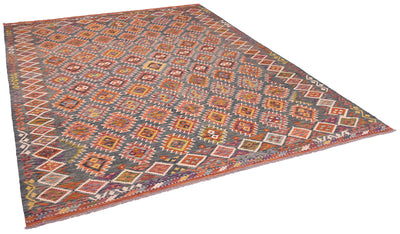 A large kilim area rug with a complex geometric pattern in green, rust red, orange, and cream, shown from an elevated perspective on a white background.