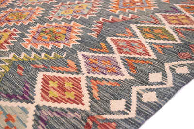 A close-up of a handwoven kilim afghan rug with a geometric tribal pattern in green, orange, red, purple, and cream.