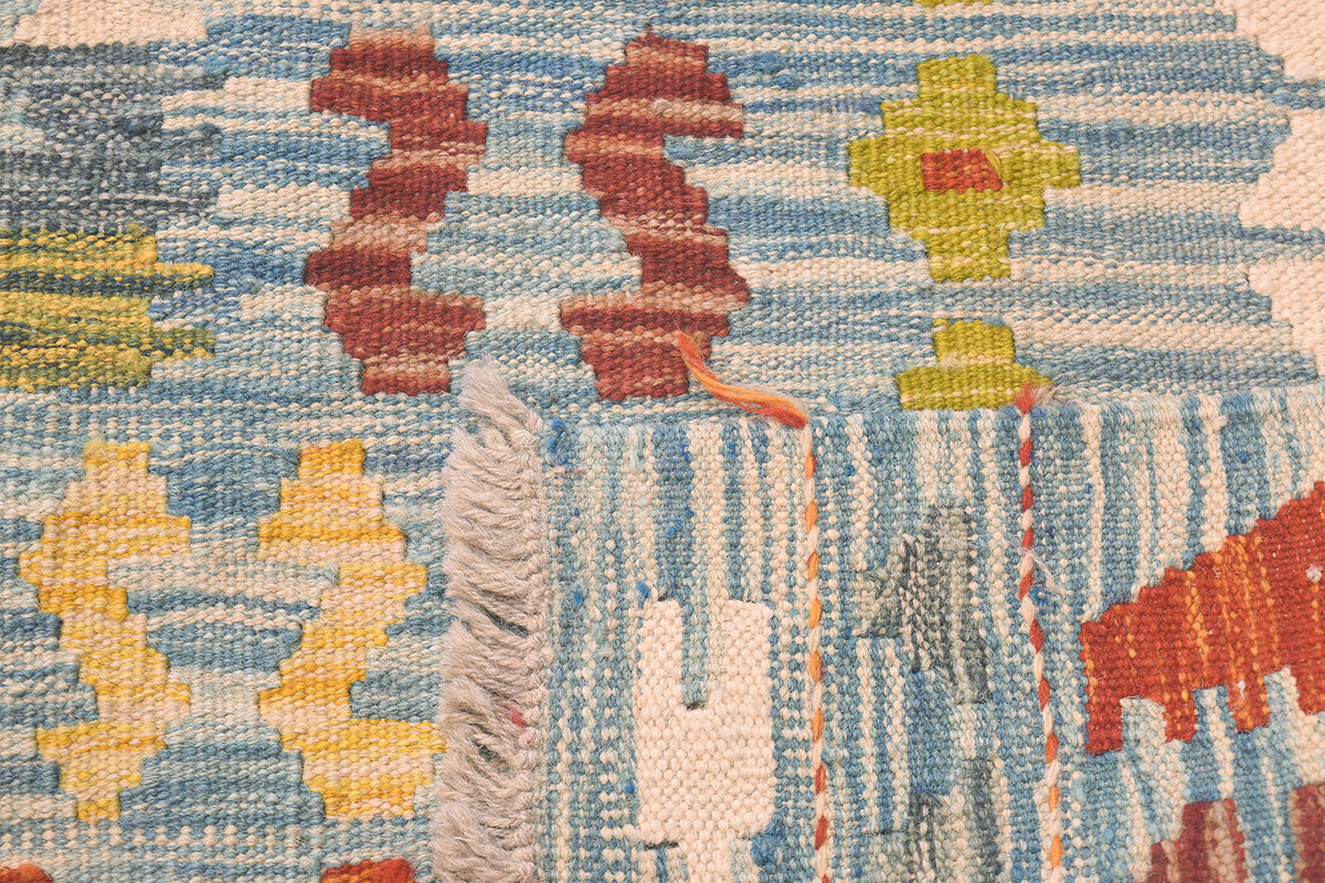 Handwoven kilim rug corner with fringe, terracotta shapes, and blue striped highlights