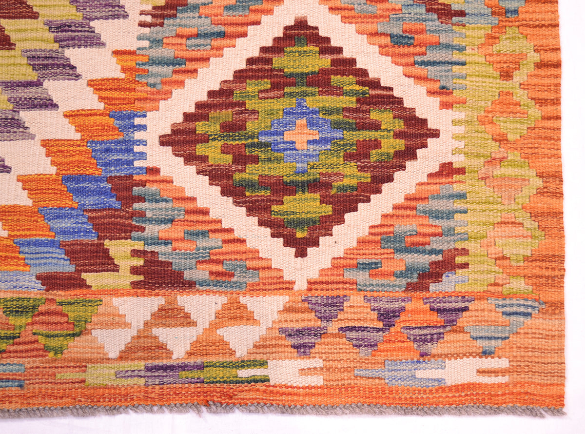 A close-up of a woven Afghan kilim rug showing a geometric diamond pattern in orange, brown, green, blue, and cream.