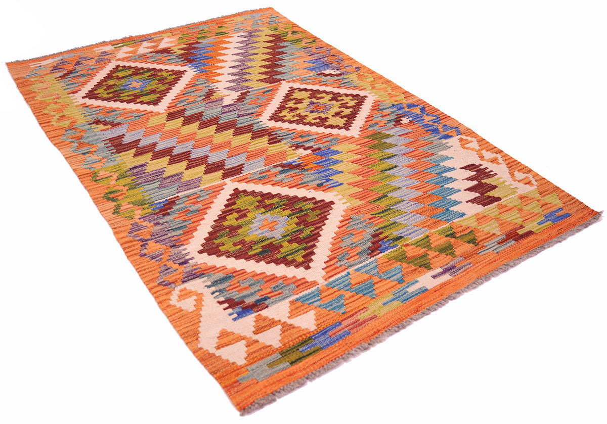A Handwoven Afghan Kilim wool rug with a vibrant geometric pattern in orange, beige, brown, green, and blue, shown from an angled perspective against a plain white background.