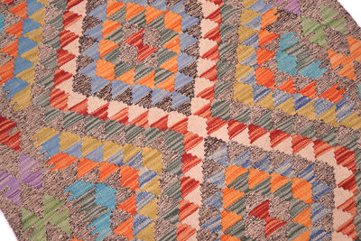 A close-up of a Afghan handwoven Kilim Rug with a multicolour geometric pattern featuring diamond and triangle motifs in orange, blue, red, green, beige, and purple.