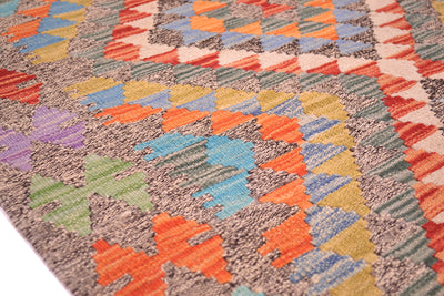 A close-up of a woven Afghan kilim rug featuring a vibrant geometric pattern with orange, blue, green, yellow, and purple shapes on a textured grey and beige background.