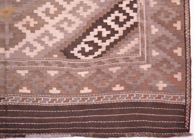 A close-up of a woven Afghan Kilim rug corner showing geometric patterns in brown, beige, and grey tones.