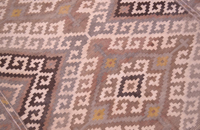 A close-up of a patterned old kilim rug with geometric tribal-style motifs in beige, brown, grey, and muted yellow.
