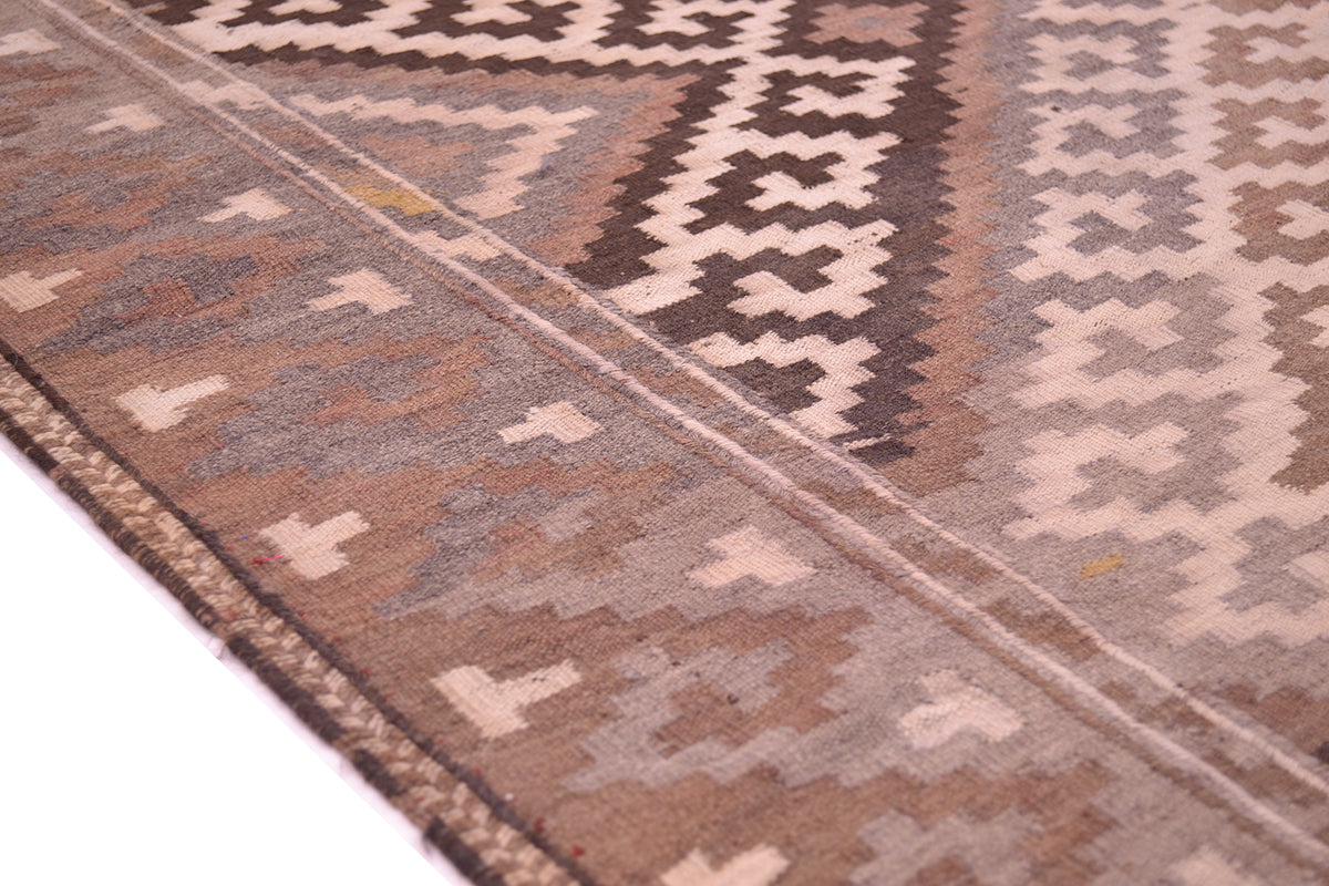 Close-up of a border from an old Afghan Kilim with geometric tribal-style motifs in brown, beige, and grey tones.