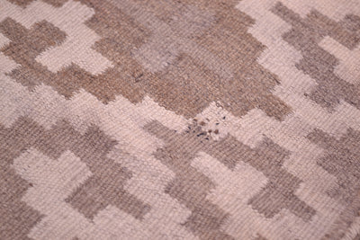 Close-up of a Kilim rug with a geometric pattern in warm taupe and light beige, showing the texture and weave detail.