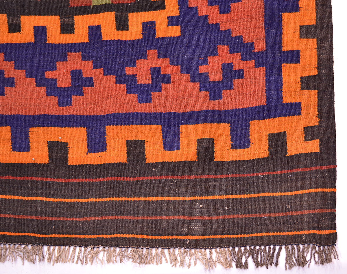 Close-up of Kilim rug border with navy and orange cross patterns; woven hem with fringe.