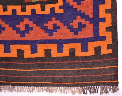 Close-up of Kilim rug border with navy and orange cross patterns; woven hem with fringe.