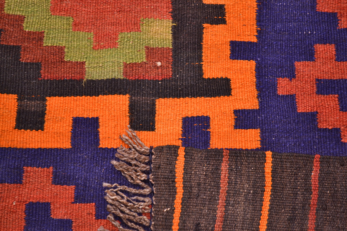 Close-up of Kilim rug motif with orange, blue, yellow, and rust blocks on dark fabric.