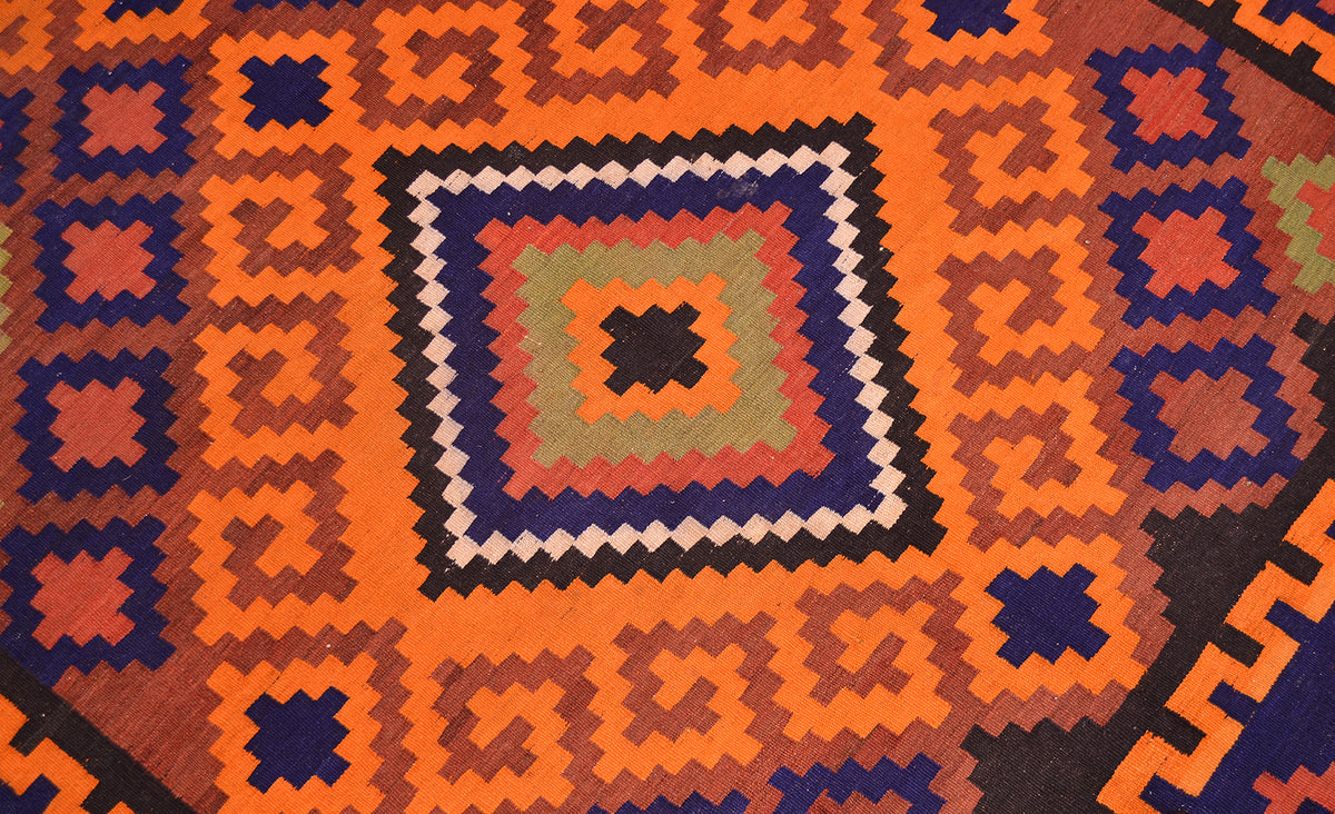 Close-up of colorful geometric Kilim rug pattern in orange, navy, and cream on dark base.