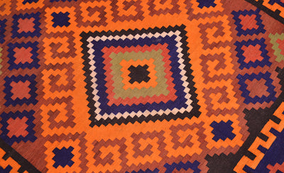 Close-up of colorful geometric Kilim rug pattern in orange, navy, and cream on dark base.