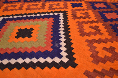 Close-up of Kilim rug weave showing orange, navy, and cream zigzags and motifs.