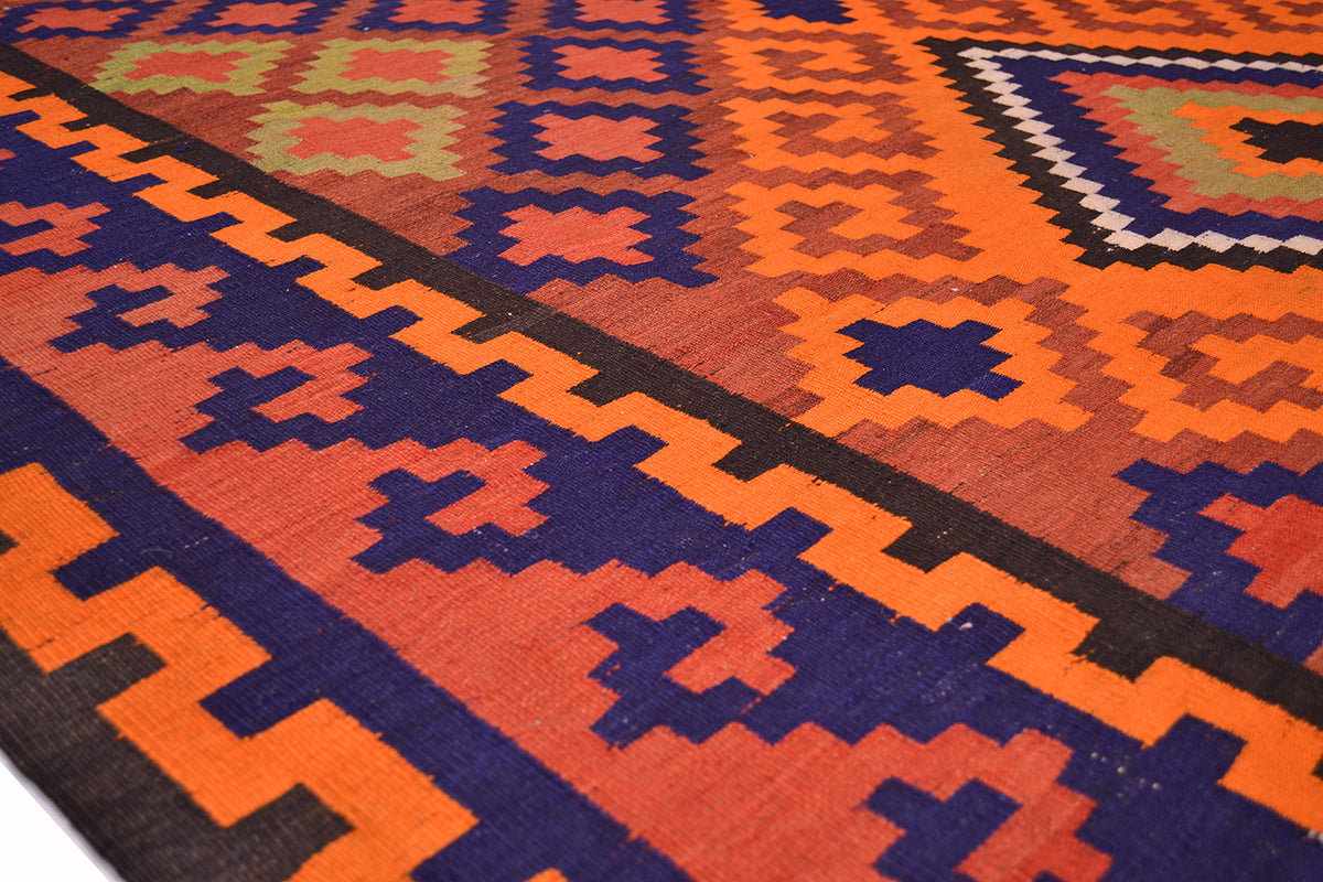 Close-up of Kilim rug corner with orange, navy, and red diamond motifs on dark ground.