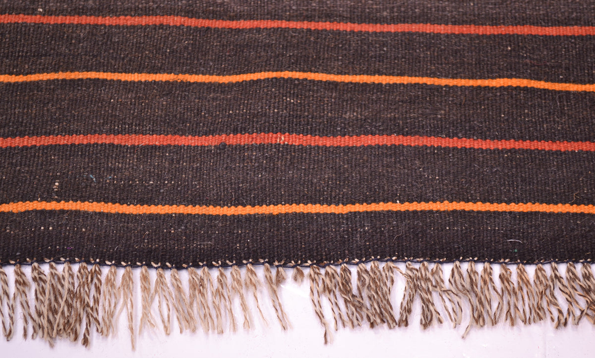 Close-up of Kilim rug edge with navy and orange stripes; cream fringe tassels.
