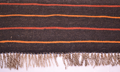 Close-up of Kilim rug edge with navy and orange stripes; cream fringe tassels.