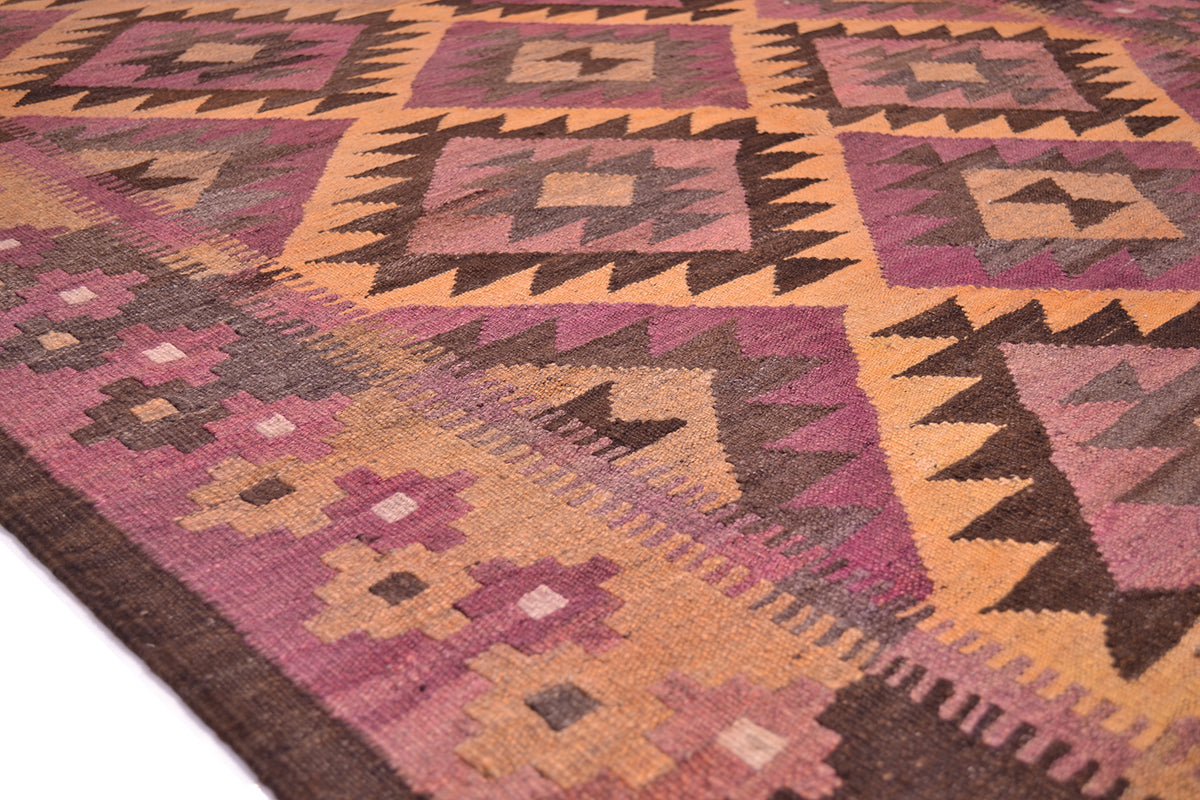 A close-up of an old handwoven geometric Afghan Kilim wide runner rug. The design features blocks of dusty pink, ochre orange, dark brown, and muted purple with intricate tribal-style motifs.