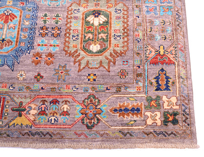 A close-up of a traditional hand-knotted Afghan area rug with a grey field, featuring a central floral medallion in green, red, and blue, surrounded by geometric borders in beige, orange, and blue.