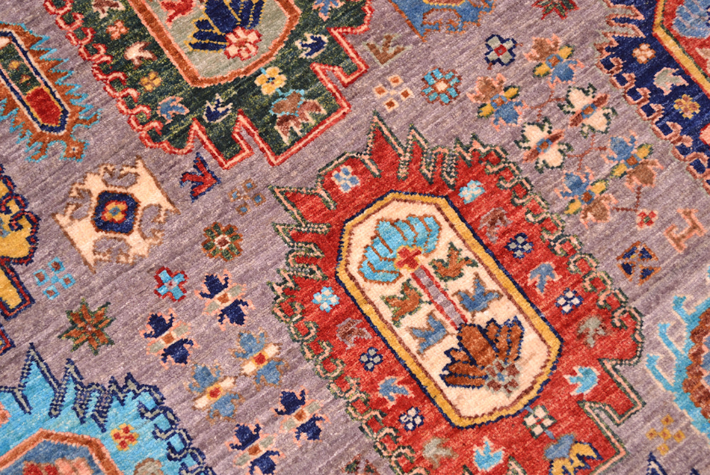 A close-up of a traditional hand-knotted Waziri area rug with a grey field, featuring a prominent red central medallion and various floral motifs in blue, green, and beige.