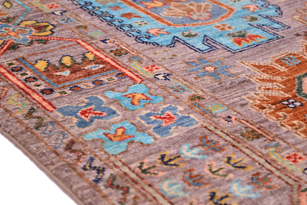 A close-up of a traditional patterned afghan Waziri rug with a grey base, featuring intricate motifs in light blue, rust orange, yellow, and dark navy.