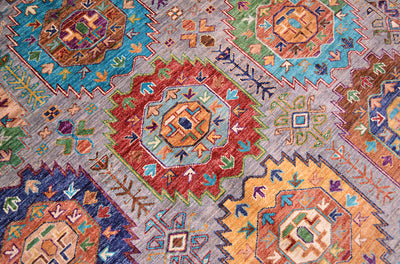 A close-up of a colourful handwoven Afghan tribal rug with traditional geometric and floral motifs in red, blue, green, orange, and beige tones.
