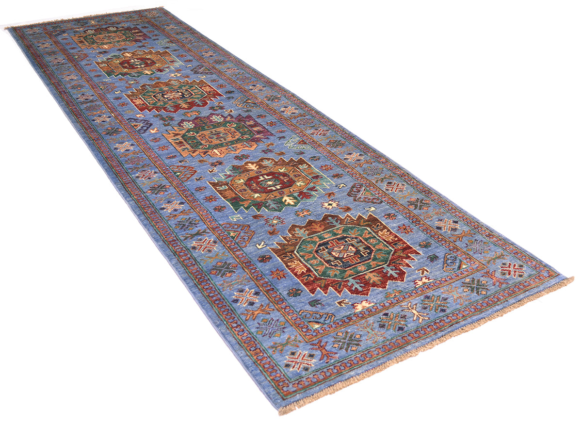 A long rectangular handmade Waziri Afghan runner with a light blue field and ornate multicoloured medallion motifs, shown on a plain white background.