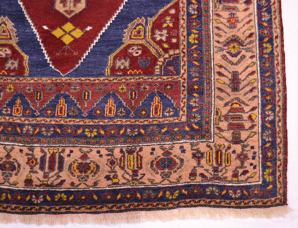 A close-up of an old oriental Turkish rug corner showing detailed woven patterns in navy blue, terracotta red, beige, and yellow.