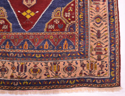 A close-up of an old oriental Turkish rug corner showing detailed woven patterns in navy blue, terracotta red, beige, and yellow.