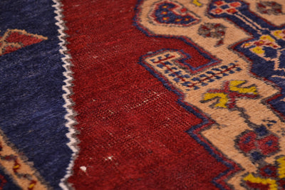Close-up of a patterned Turkish rug showing a deep red field, a navy blue section with a white zigzag border, and beige sections with blue and yellow ornamental motifs.