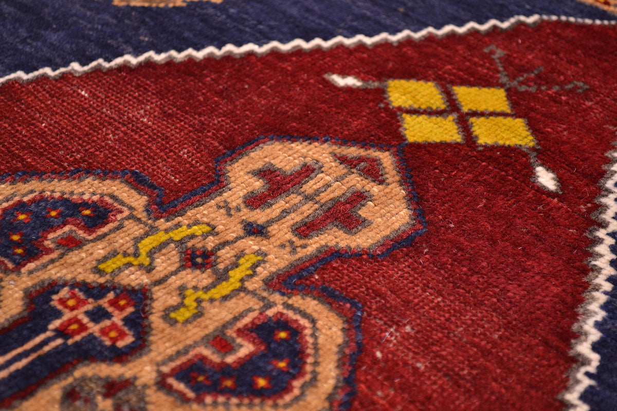Close-up of an old Turkish handwoven rug with a deep red field, cream central motif, navy blue corner sections, and yellow geometric accents.