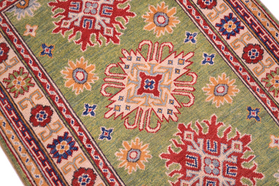Green wool rug close-up, red and orange starburst motifs with blue accent details