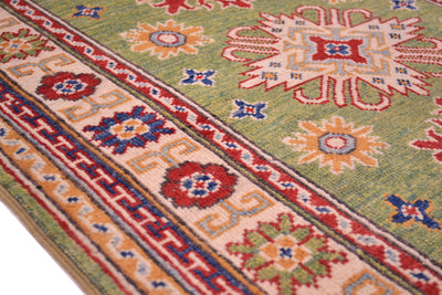 Green wool rug border close-up with red, blue, and orange diamond motif band