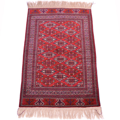 A traditional rectangular hand-knotted Turkoman Yamoud wool rug with a vibrant red field, intricate geometric and floral motifs, and cream-coloured fringe on the top and bottom edges.