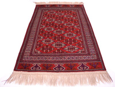 A traditional handmade red Turkoman wool rug with an intricate geometric pattern and cream-coloured fringe on the top and bottom edges, displayed flat against a white background.
