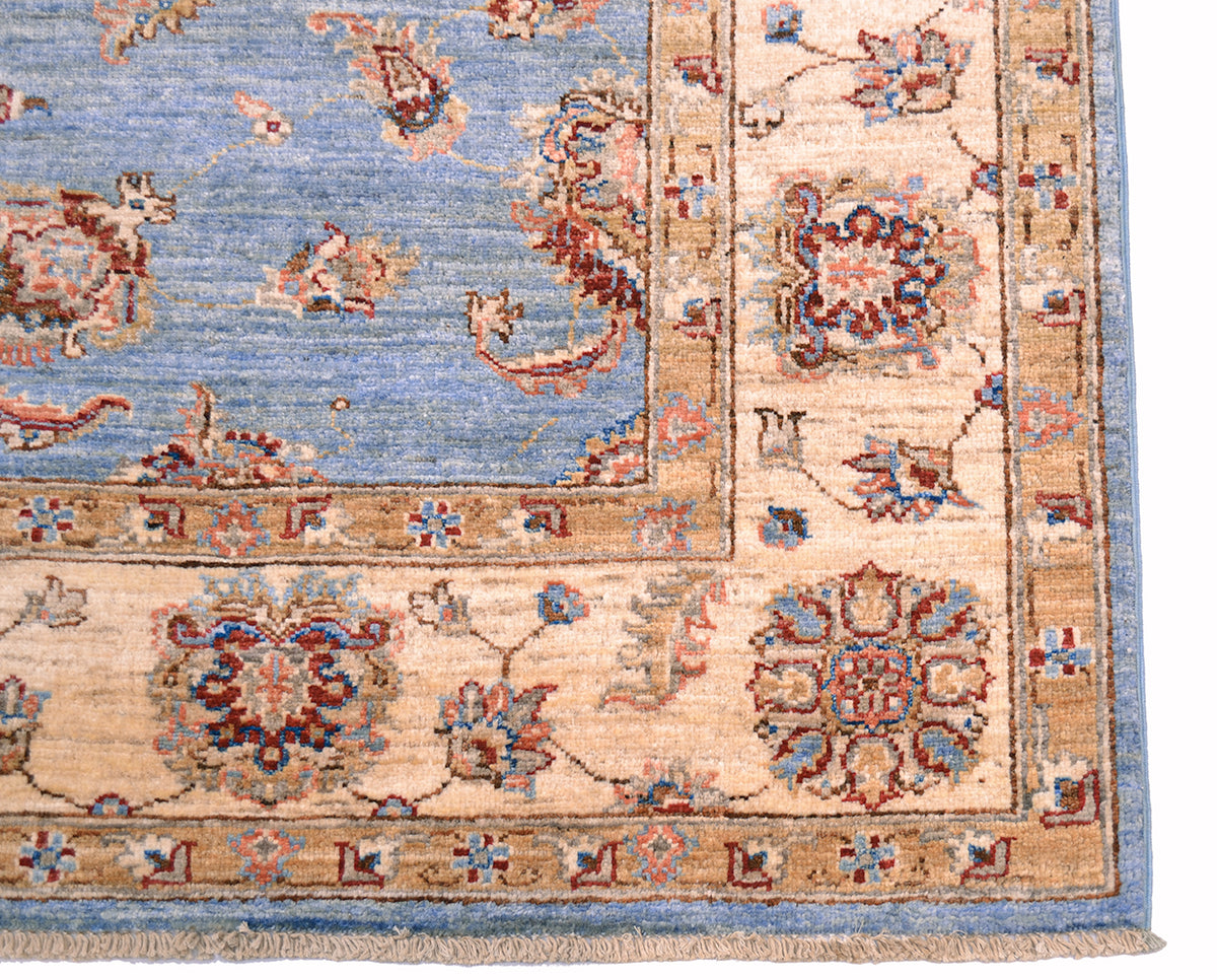 Corner detail of handmade carpet in cream and blue with cotton warp fringes.