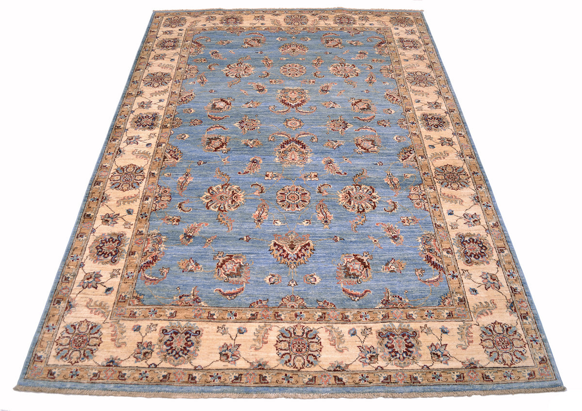 Floating flowers in light blue field of handmade afghan carpet with cream and golden beige border.