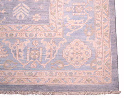 Corner of pastel blue patterned rug with pinkish border trim and fringe