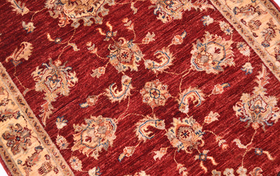 Detailed view of main field of handknotted rug with palmettes in blue, cream and terracotta on a red russet field.