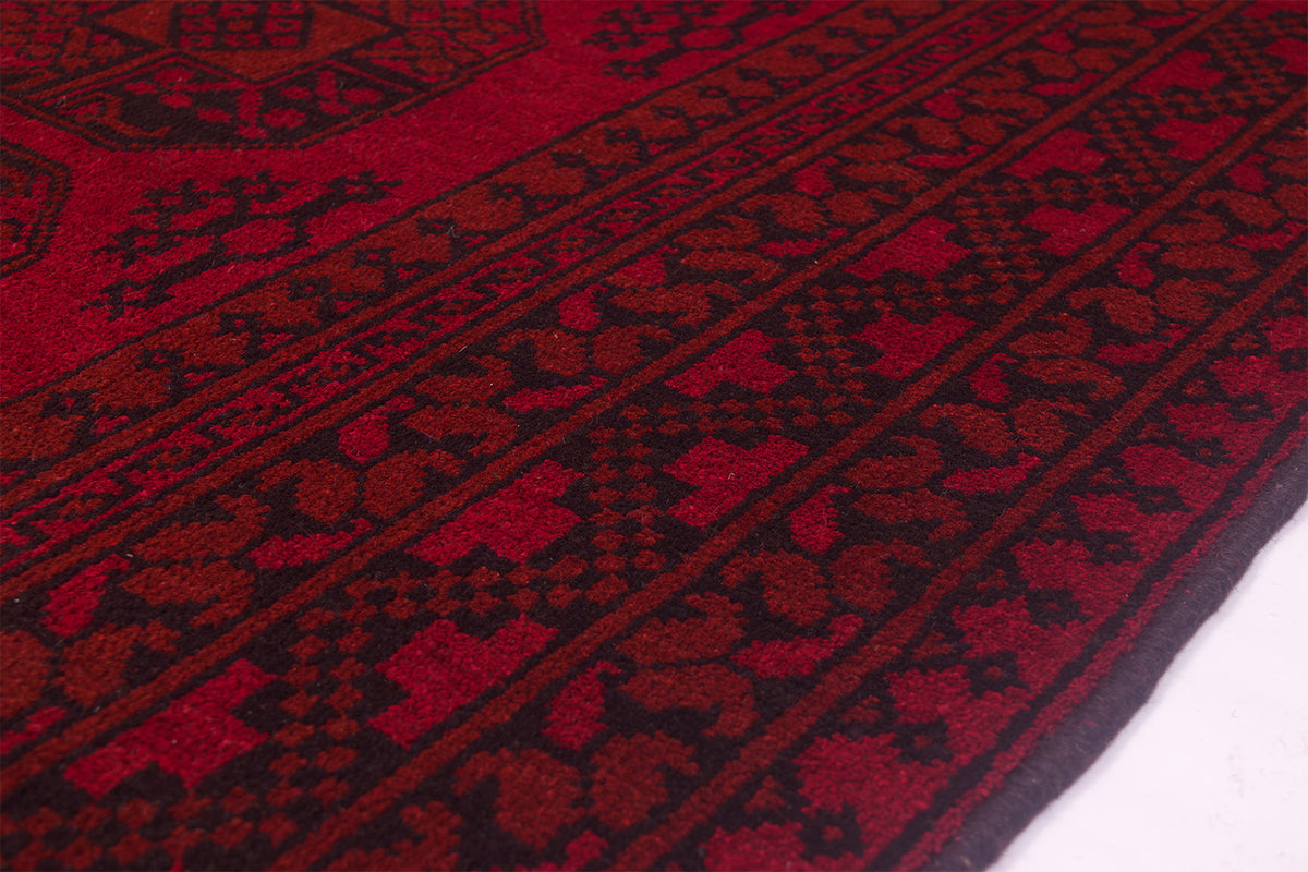 A close-up of a handmade red and black patterned Afghan carpet showing detailed woven geometric and floral motifs.