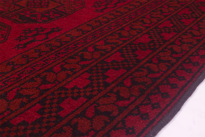 A close-up of a handmade red and black patterned Afghan carpet showing detailed woven geometric and floral motifs.