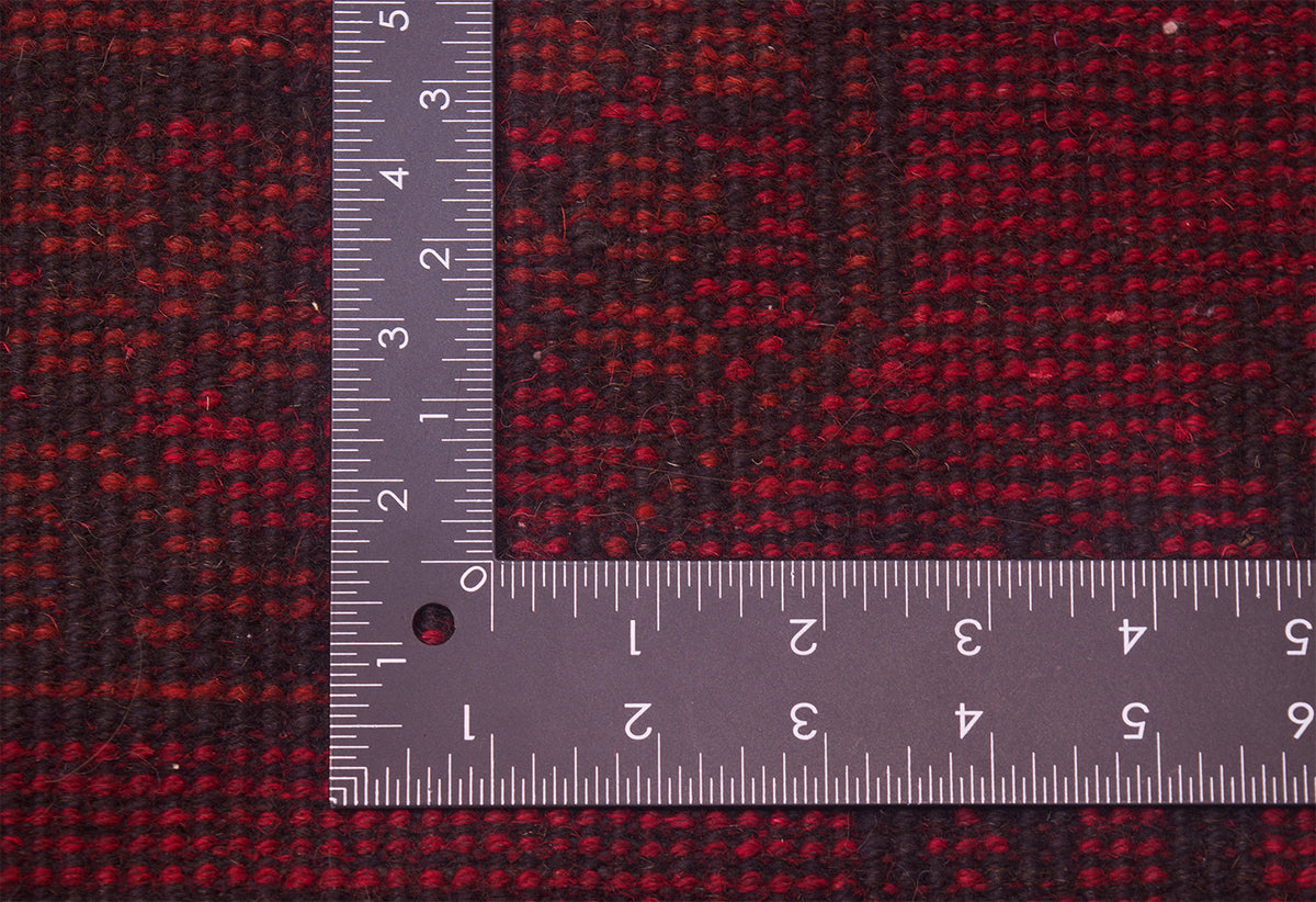 A close-up the hand-knotted back of a red and black Afghan Aqcha Carpet with a metal L-square ruler placed on top to show the scale of the knotting.